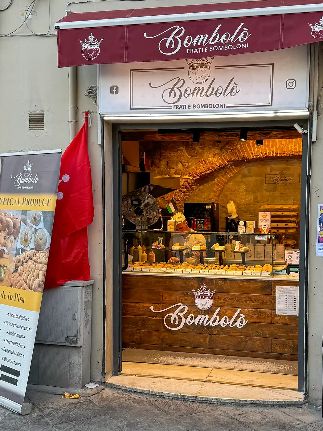 Eine Konditorei namens „Bombolò“ mit einer Auslage voller Gebäck und einer roten Markise über dem Eingang.