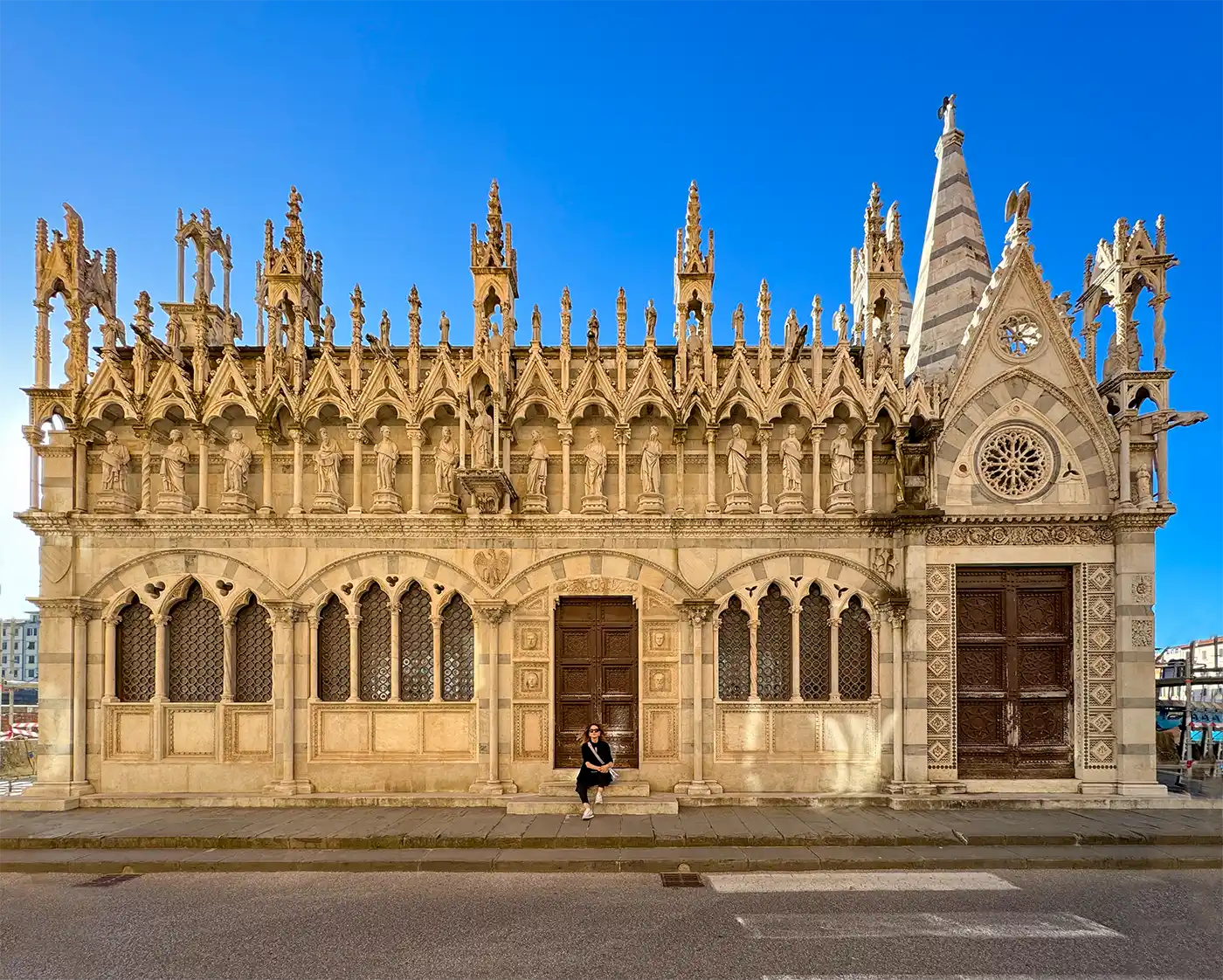 Kirchenfassade im gotischen Stil aus Marmor mit Spitzbögen, Statuen und einer auf den Stufen sitzenden Person.