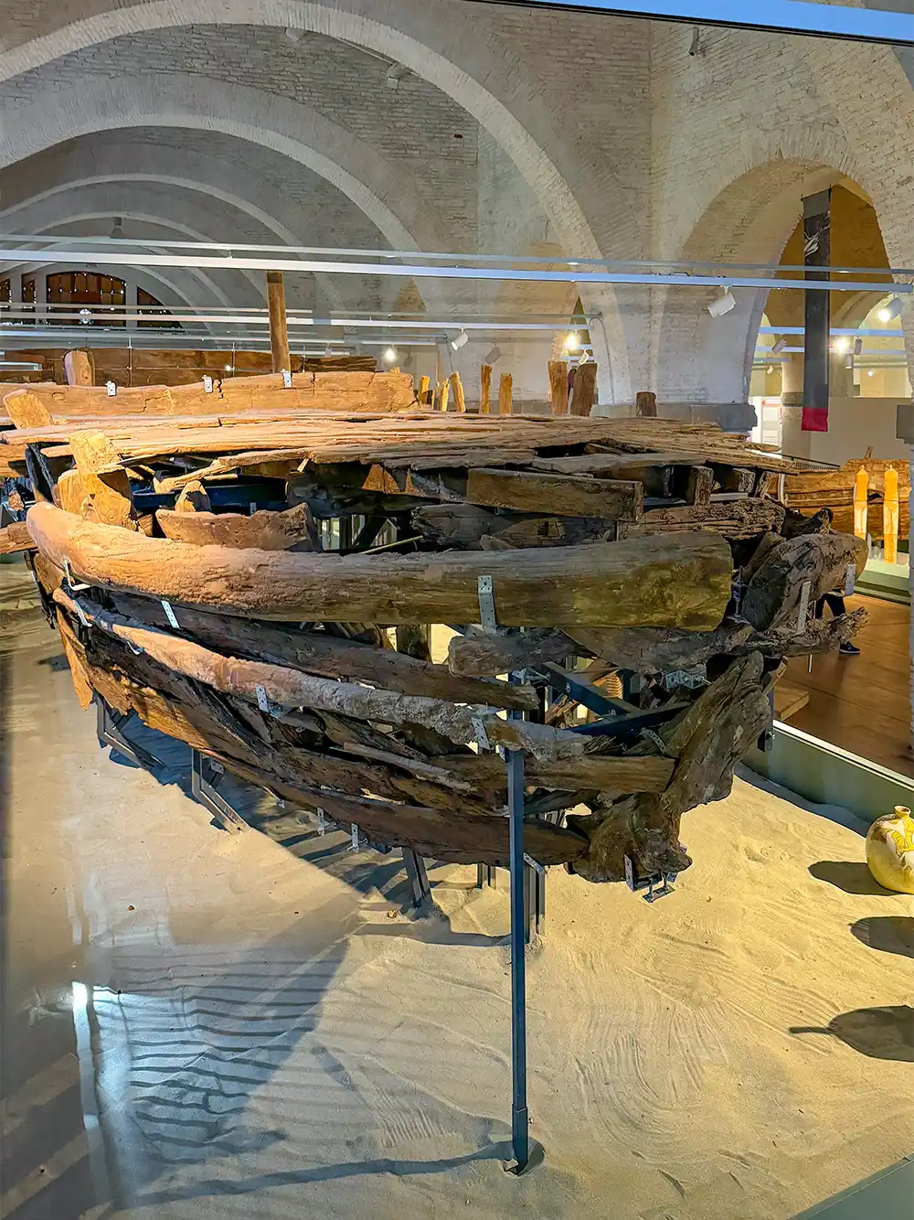 Ein antikes Holzschiffwrack, ausgestellt auf Metallstützen in einem Museum mit gewölbten Decken und heller Beleuchtung.