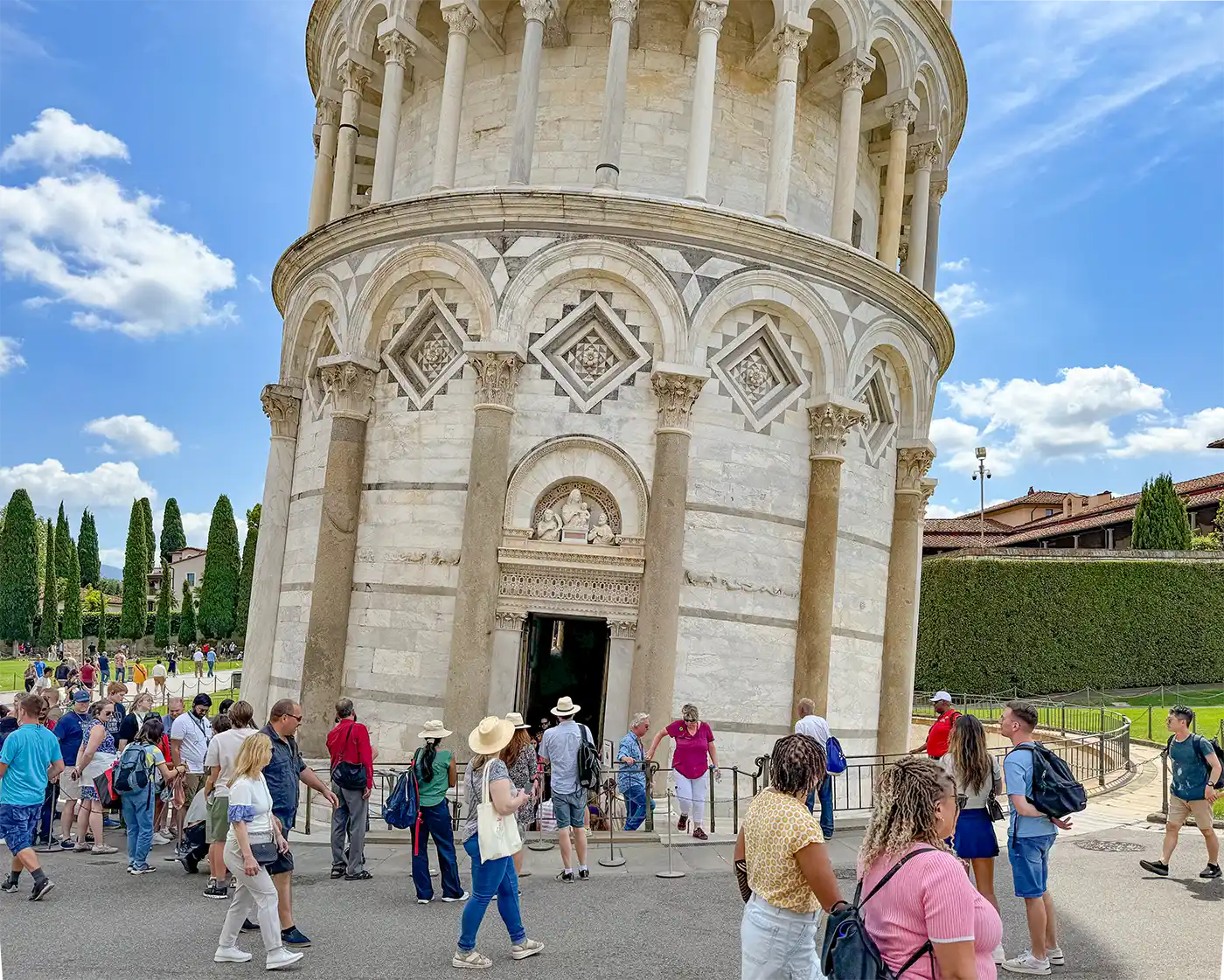 Schiefer-Turm-von-Pisa An einem sonnigen Tag versammeln sich Touristen am Eingang des säulenbekränzten Turms von Pisa.