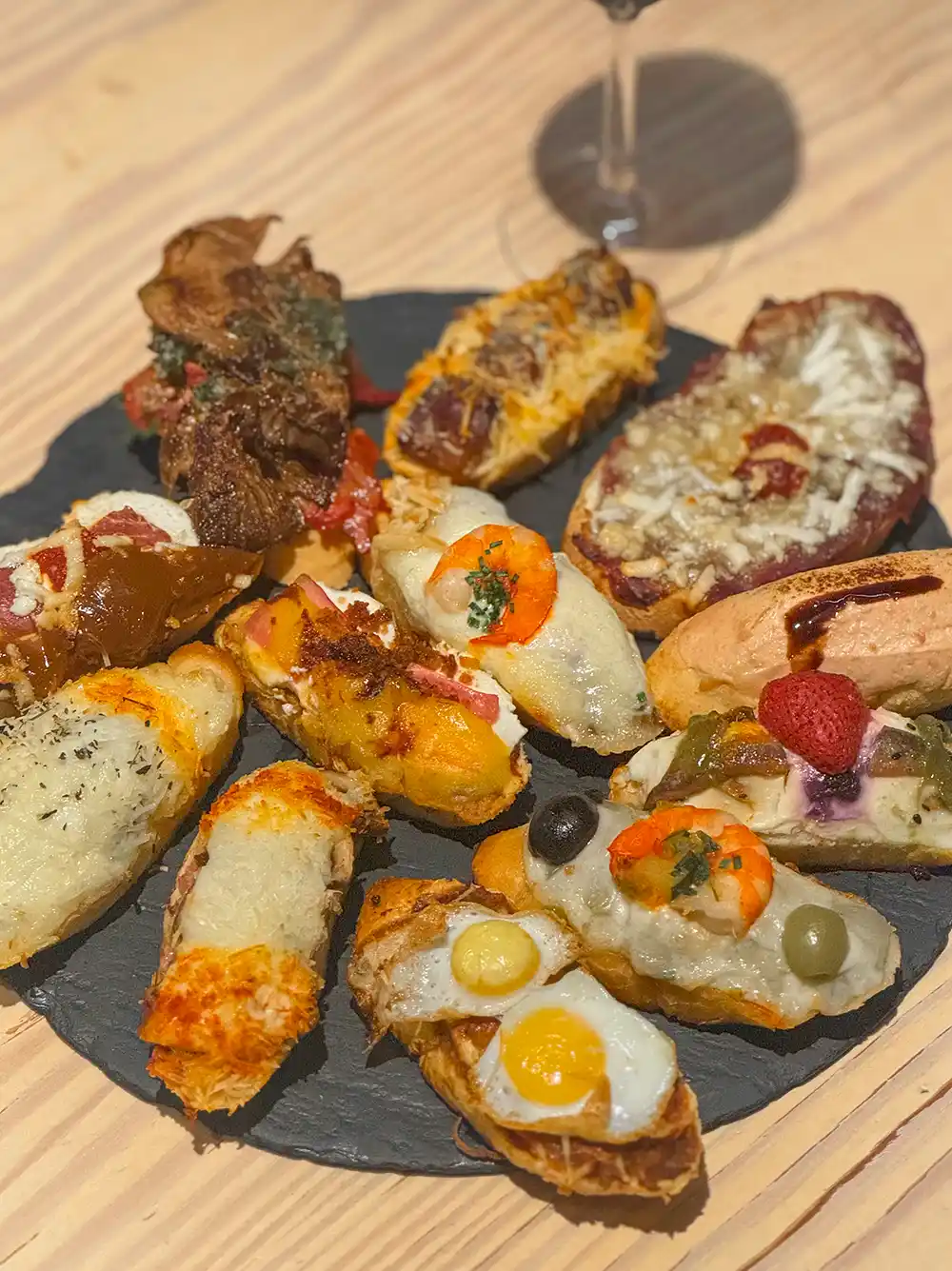 Valladolid-Brot-Tapas-Jero Eine Schieferplatte mit verschiedenen Pintxos, darunter Käse, Eier, Oliven, Gemüse und Fleisch auf Brot.