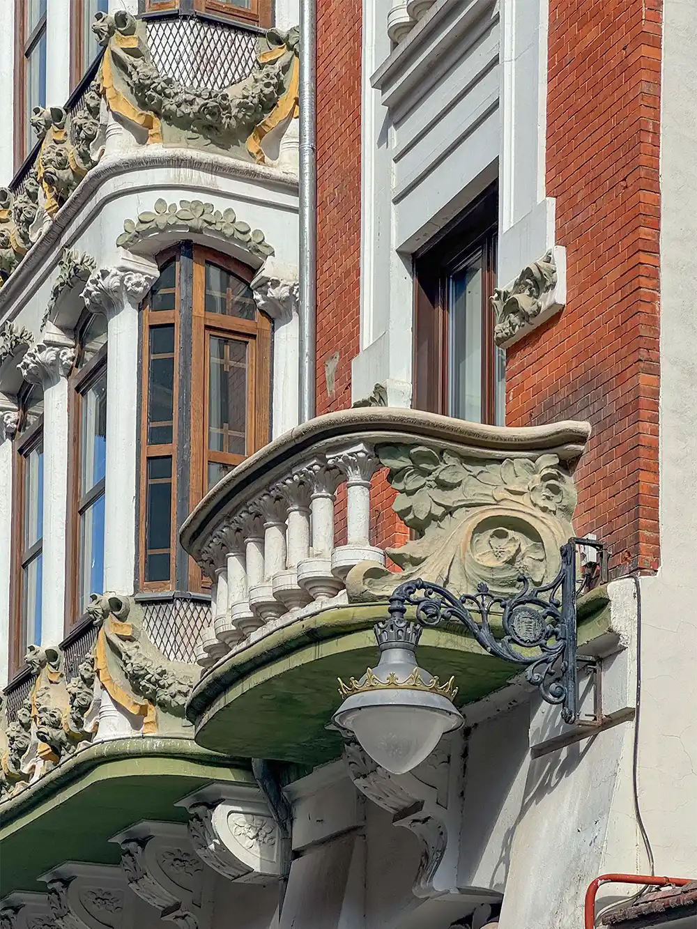 Valladolid-Casa-del-Principe-Detail Ein kunstvoll verzierter Balkon mit skulpturalen Details und einer Straßenlaterne an der Fassade eines Backsteingebäudes.