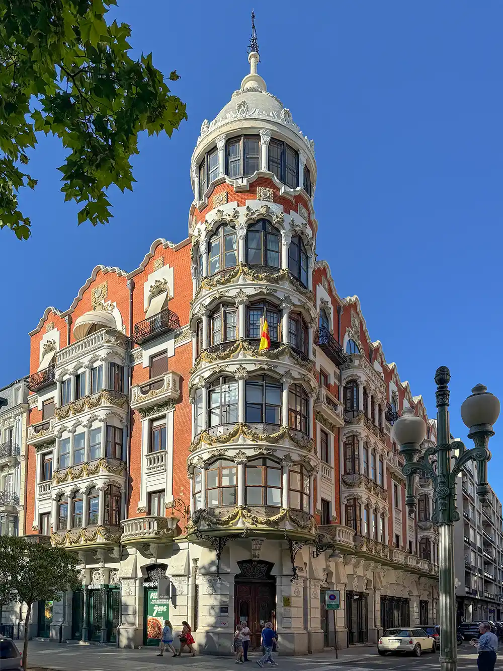 Valladolid-Casa-del-Principe Ein prunkvolles historisches Gebäude mit rot-weißer Fassade, einem runden Turm und Balkonen an einer sonnigen Straßenecke.