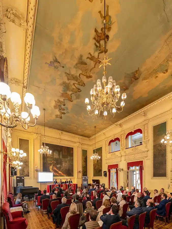 Valladolid-Circulo-de-recreo-Hauptsaal Ein prächtiger Saal mit Kronleuchtern, bemalter Decke, einer Rednerbühne und dem Publikum, das darunter sitzt.