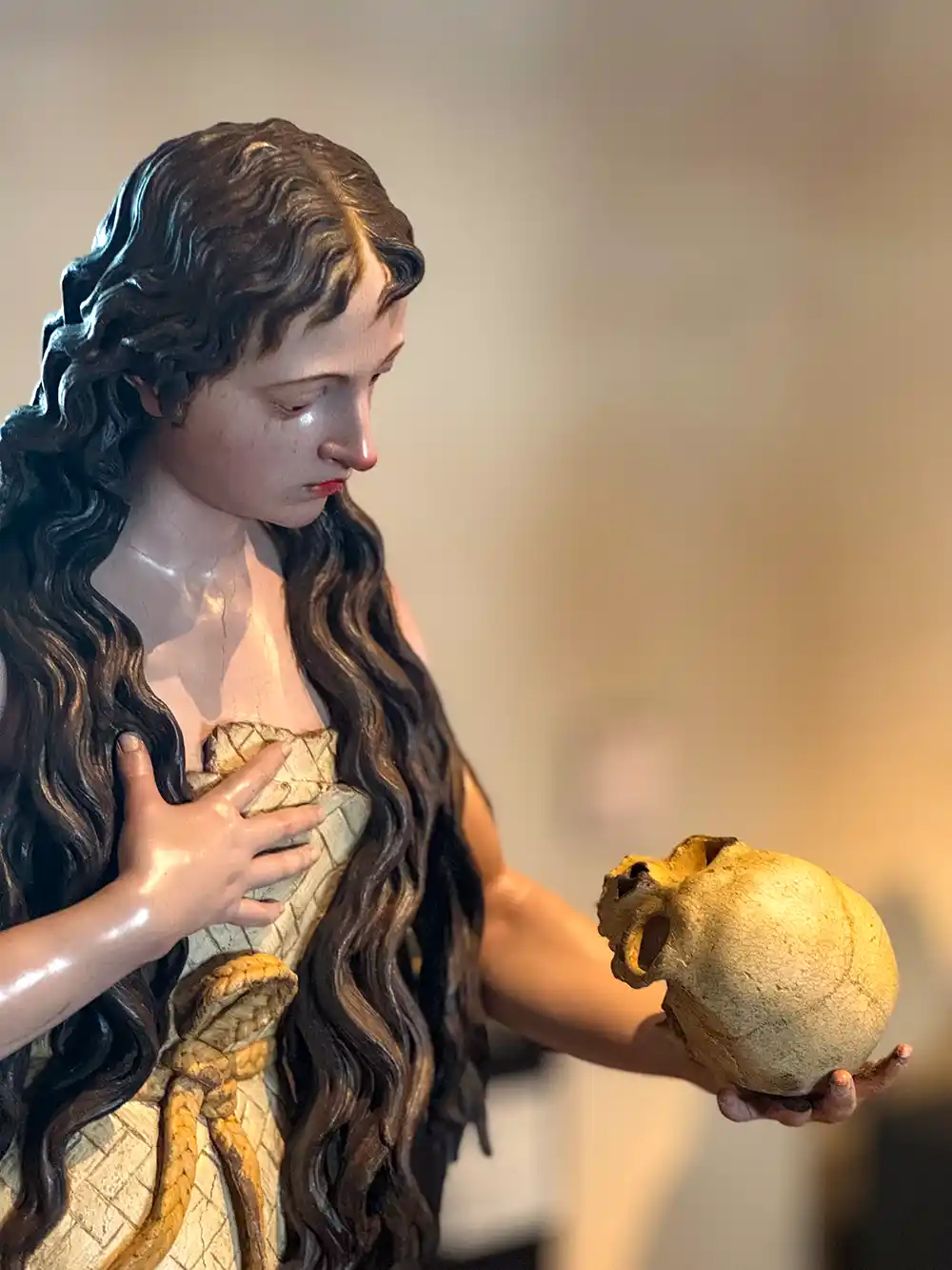 Valladolid-Colegio-San-Gregorio-Holz-Skulptur Eine lebensechte Statue einer Frau mit langen Haaren, die einen Schädel in der Hand hält und ihn nachdenklich betrachtet.