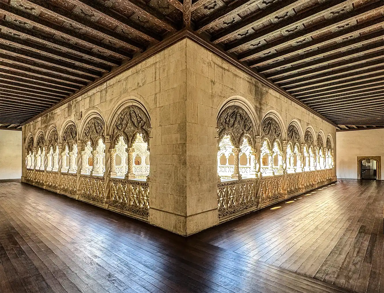 Valladolid-Colegio-San-Gregorio-Stockwerk Kunstvoll verzierte Steinbögen mit aufwendigen Schnitzereien und Holzböden in einem sonnendurchfluteten, historischen Innenraum in Valladolid.