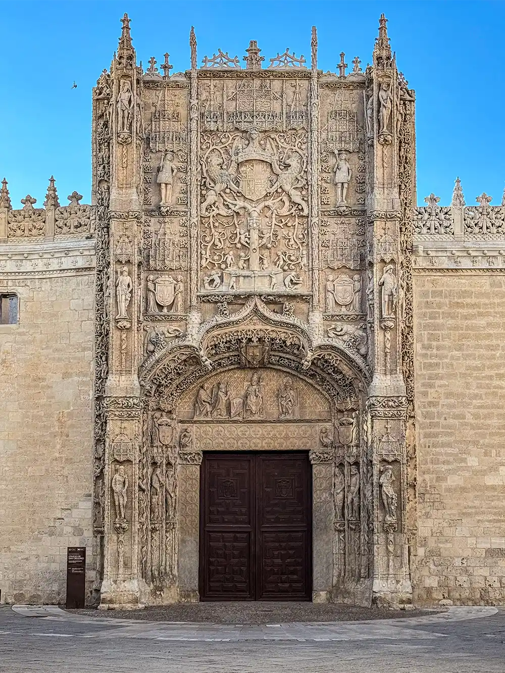 Valladolid-Colegio-San-Gregorio Der kunstvoll verzierte Steineingang eines historischen Gebäudes mit detailreichen Schnitzereien vor einem strahlend blauen Himmel.