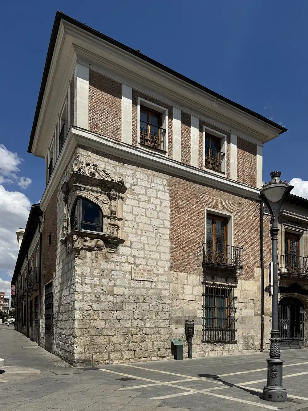 Valladolid-Palacio-Pimentel-Eckfenster Historisches dreistöckiges Backstein- und Steingebäude mit kunstvoll verzierten Fenstern unter strahlend blauem Himmel.