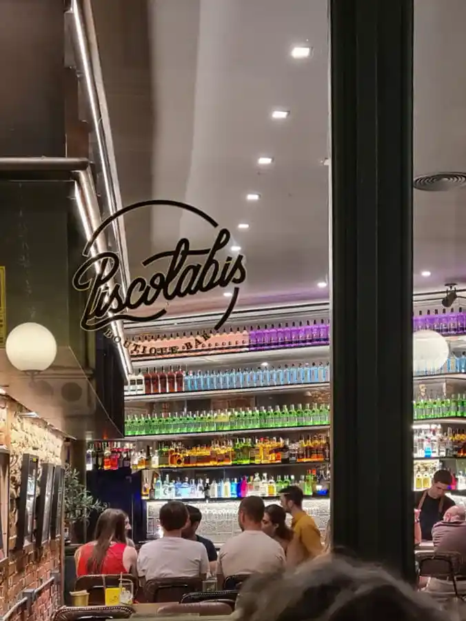 Valladolid-Pasaje-Gutierrez-Piscolabis Eine Gruppe von Leuten sitzt in einer Bar, in der bunte Flaschen in den Regalen stehen