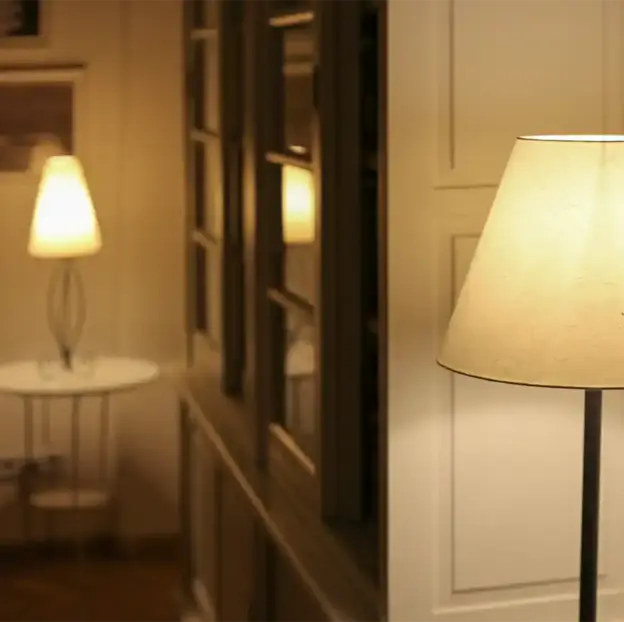Zwei warm leuchtende Lampen, eine nah und eine fern, erhellen einen Flur mit cremefarbenen Wänden und gerahmten Fenstern.