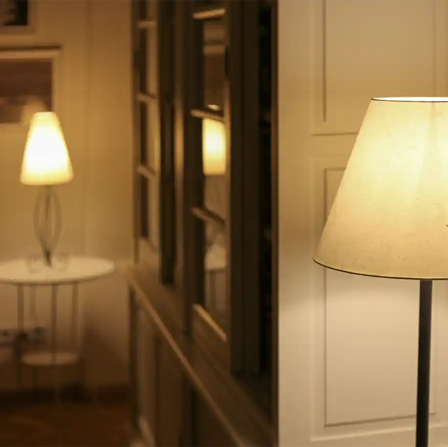 Zwei warm leuchtende Lampen, eine nah und eine fern, erhellen einen Flur mit cremefarbenen Wänden und gerahmten Fenstern.