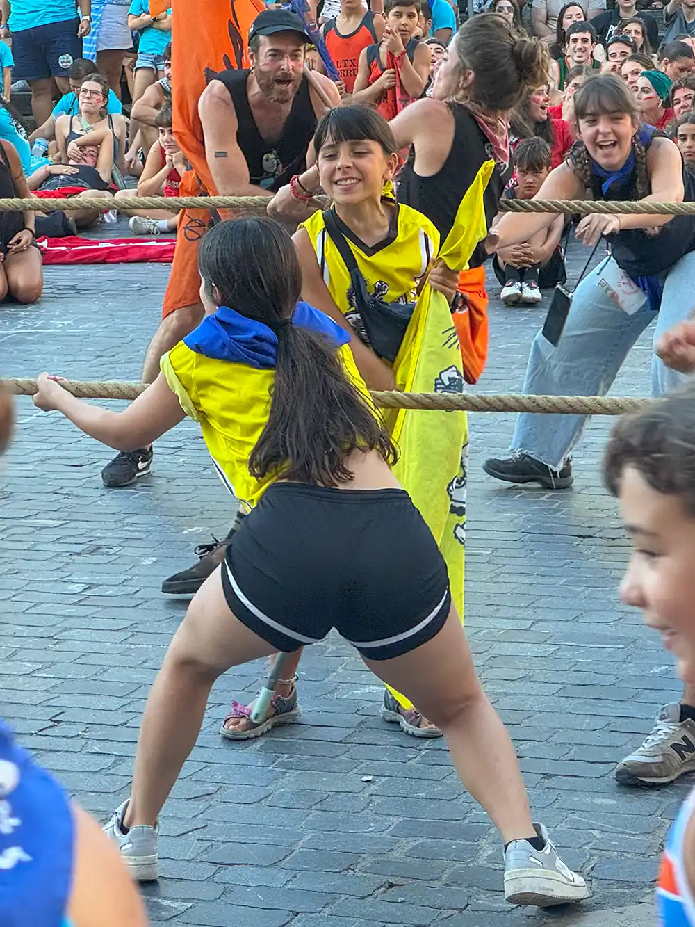 Aste-Nagusia-Bilbao-Tauziehen Kinder in gelben T-Shirts spielen draußen Tauziehen und werden dabei von einer Menge begeisterter Zuschauer angefeuert.