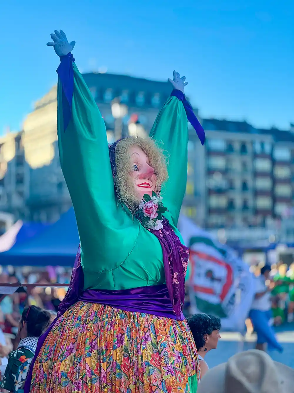 Aste-Nagusia-Marijaia Eine Person in einem bunten, übergroßen Kostüm, die bei einem Open-Air-Festival die Arme hochreckt.