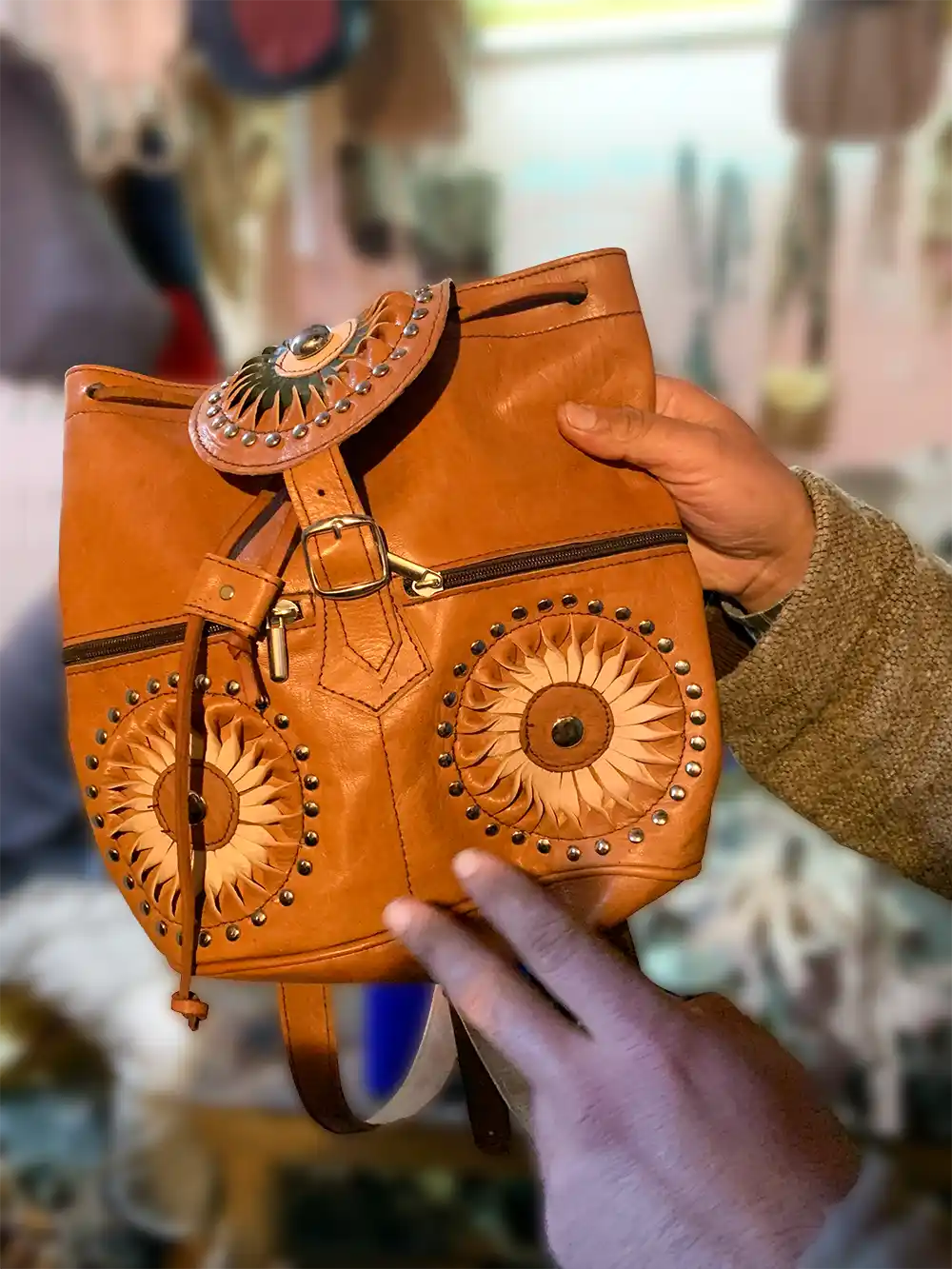 Basar-Ledertasche Eine Person hält einen braunen Lederrucksack mit kreisförmigen Mustern und Metallnieten in der Hand, der dem Gesicht einer Eule ähnelt.