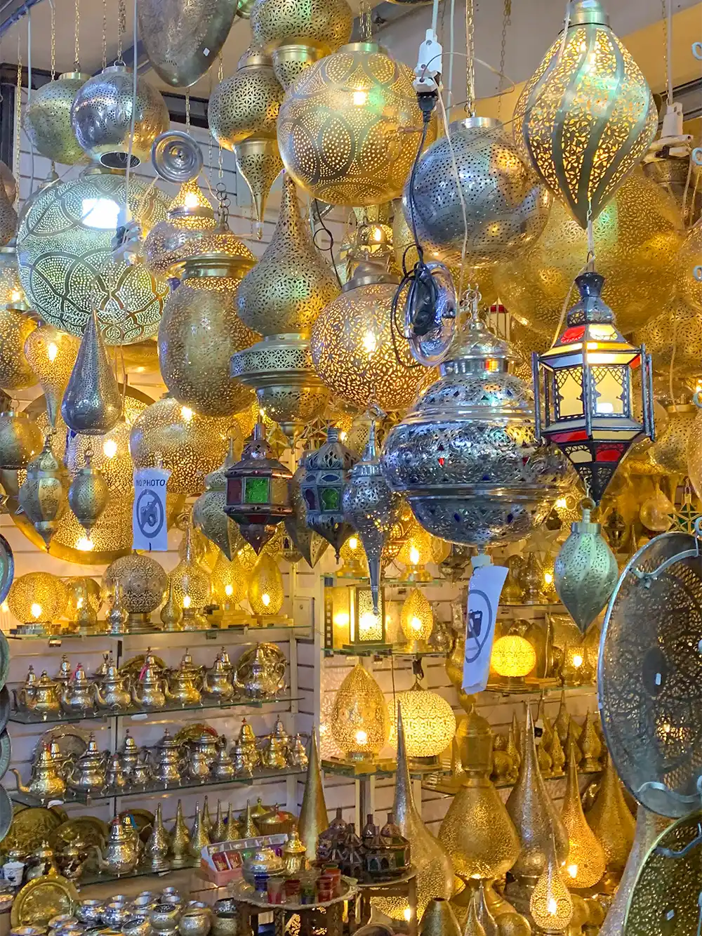 Bazar-Feilschen-Lampen An einem überfüllten Marktstand, an dem Zierlampen verkauft werden, hängen goldene und silberne Laternen und leuchten.