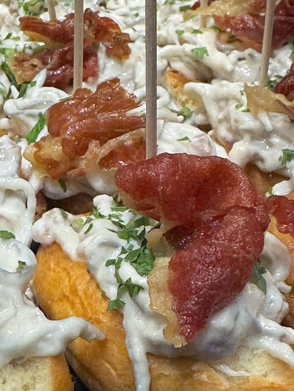 Bilbao-Pintxo-Bars-Victor-Monztes-Jamon Geröstetes Brot, belegt mit cremiger Soße, knusprigem Speck und gehackter Petersilie, zusammengehalten mit Zahnstochern.