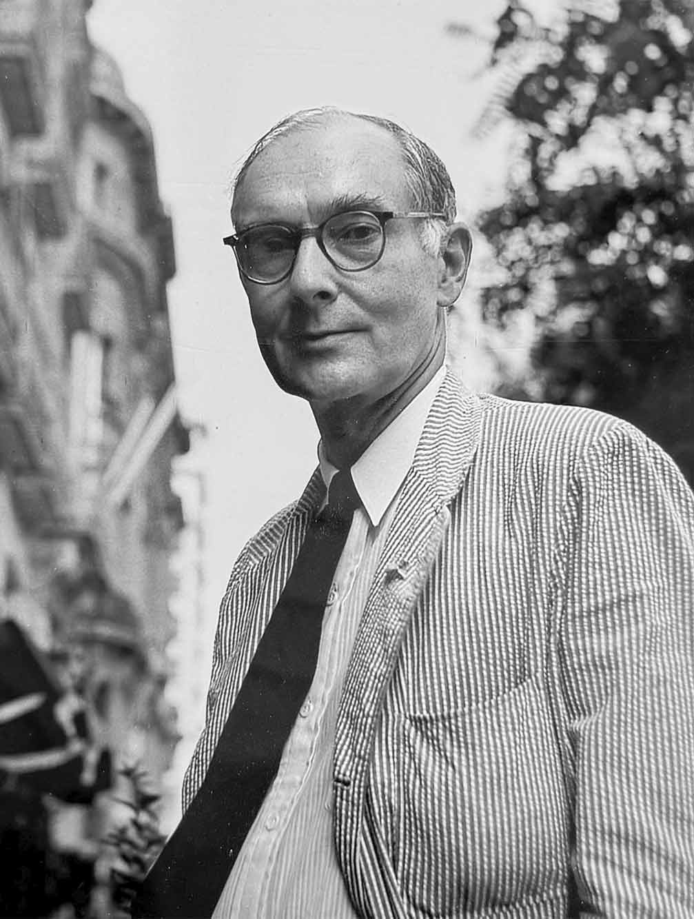 Cuenca-Fernando-Zobel Ein Mann mit Brille und gestreifter Jacke steht draußen in der Nähe eines Gebäudes und blickt in die Kamera.