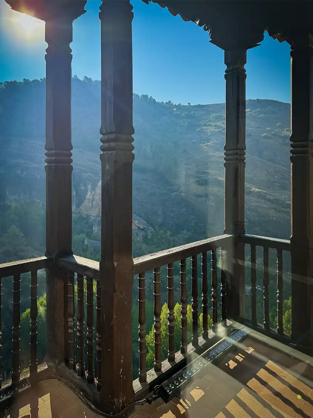 Cuenca-Haengende-Haeuser-Balkon Der sonnendurchflutete Holzbalkon bietet einen Blick auf bewaldete Hügel und Berge unter einem strahlend blauen Himmel.