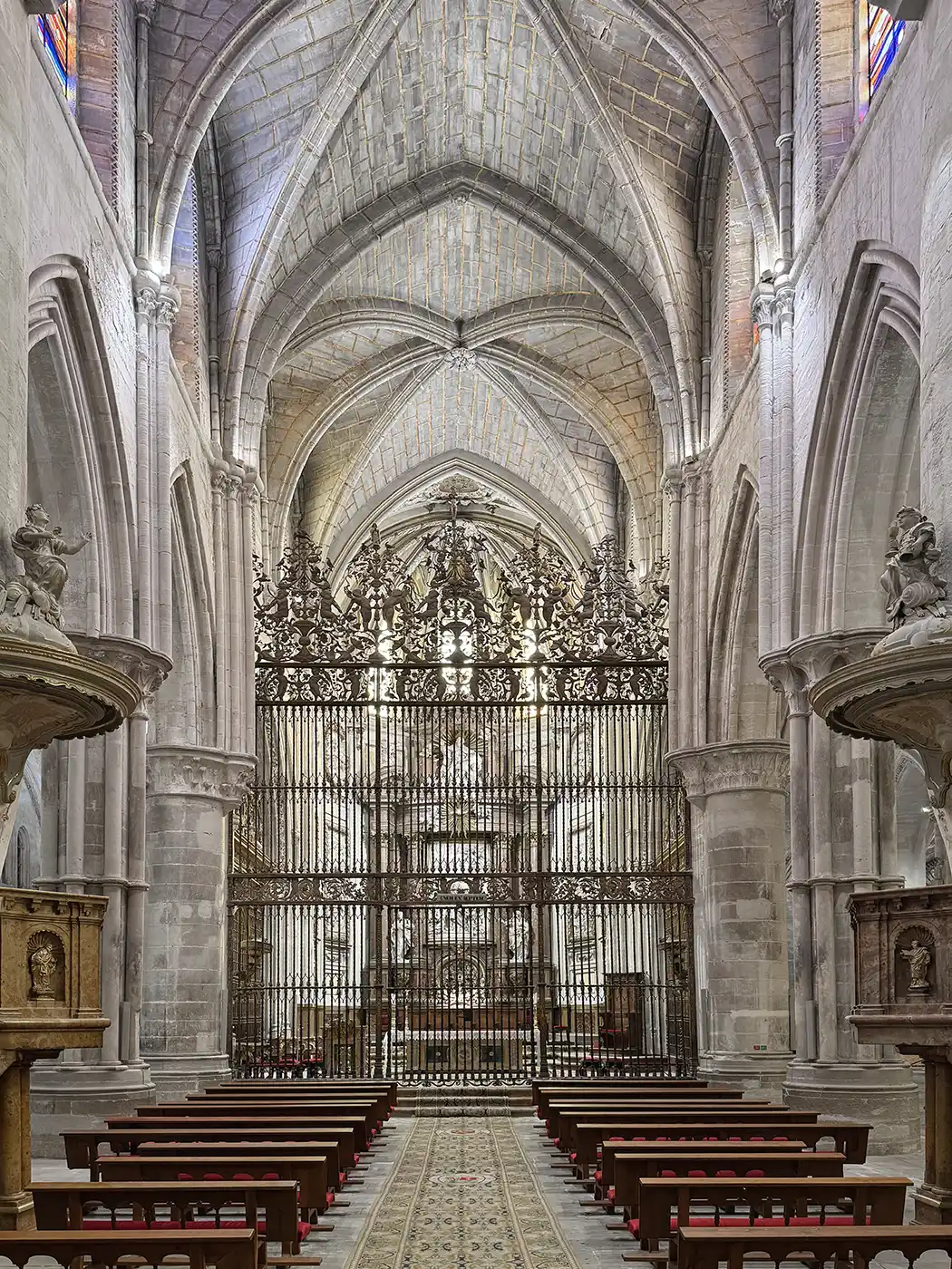 Cuenca-Kathedrale-innen Innenraum einer gotischen Kathedrale mit Gewölbedecke, Kirchenbänken, einem kunstvoll verzierten Eisentor und detailreichen Steinbögen.