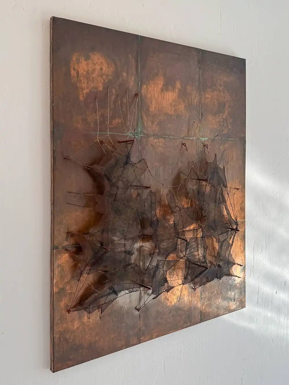 Cuenca-Manuel-Rivera-Metamorfosis-1962 Abstraktes Mixed-Media-Kunstwerk mit kupferfarbenen Paneelen und dunklem Netzgewebe, das Schatten auf eine weiße Wand wirft.
