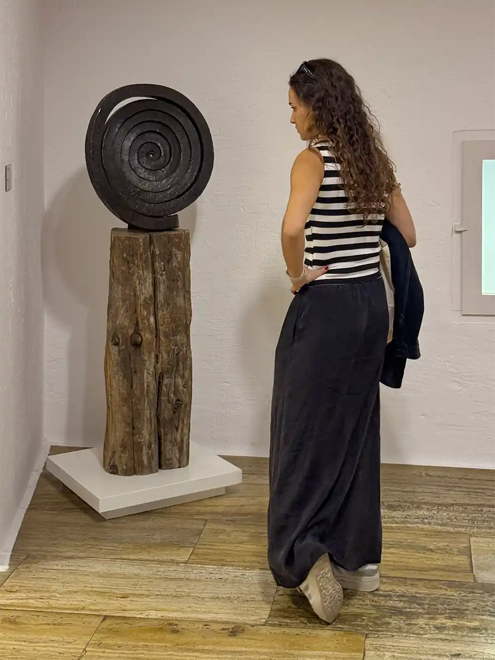 Cuenca-Museum-abstrakte-Kunst-Skulptur Eine Frau steht in einer Kunstgalerie vor einer spiralförmigen Skulptur auf einem Holzsockel und wendet dem Betrachter den Rücken zu.