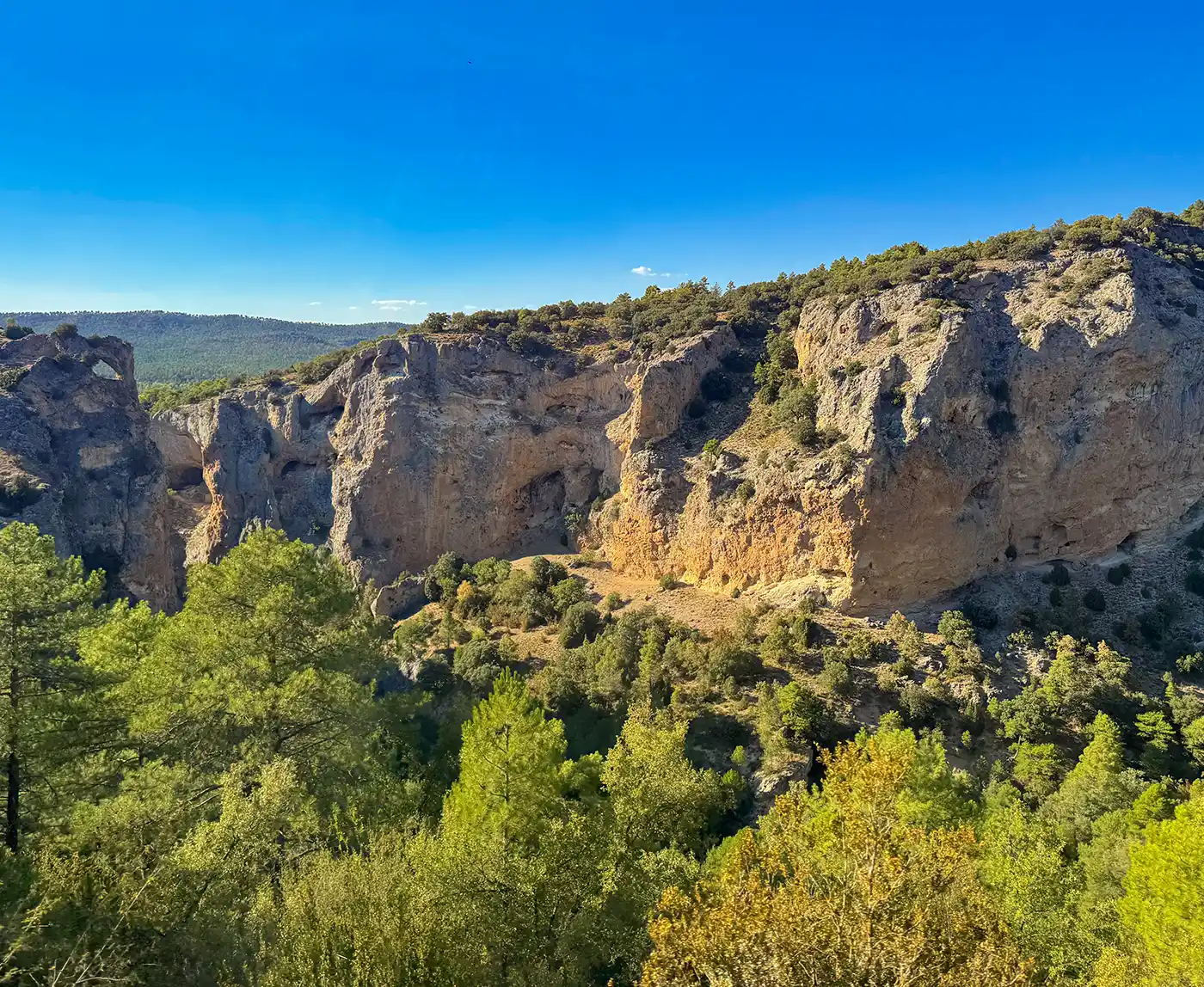 Cuenca-Naturpark- Serrania-de-Cuenca Felsige Klippen mit grünen Kiefern unter einem strahlend blauen Himmel an einem sonnigen Tag.