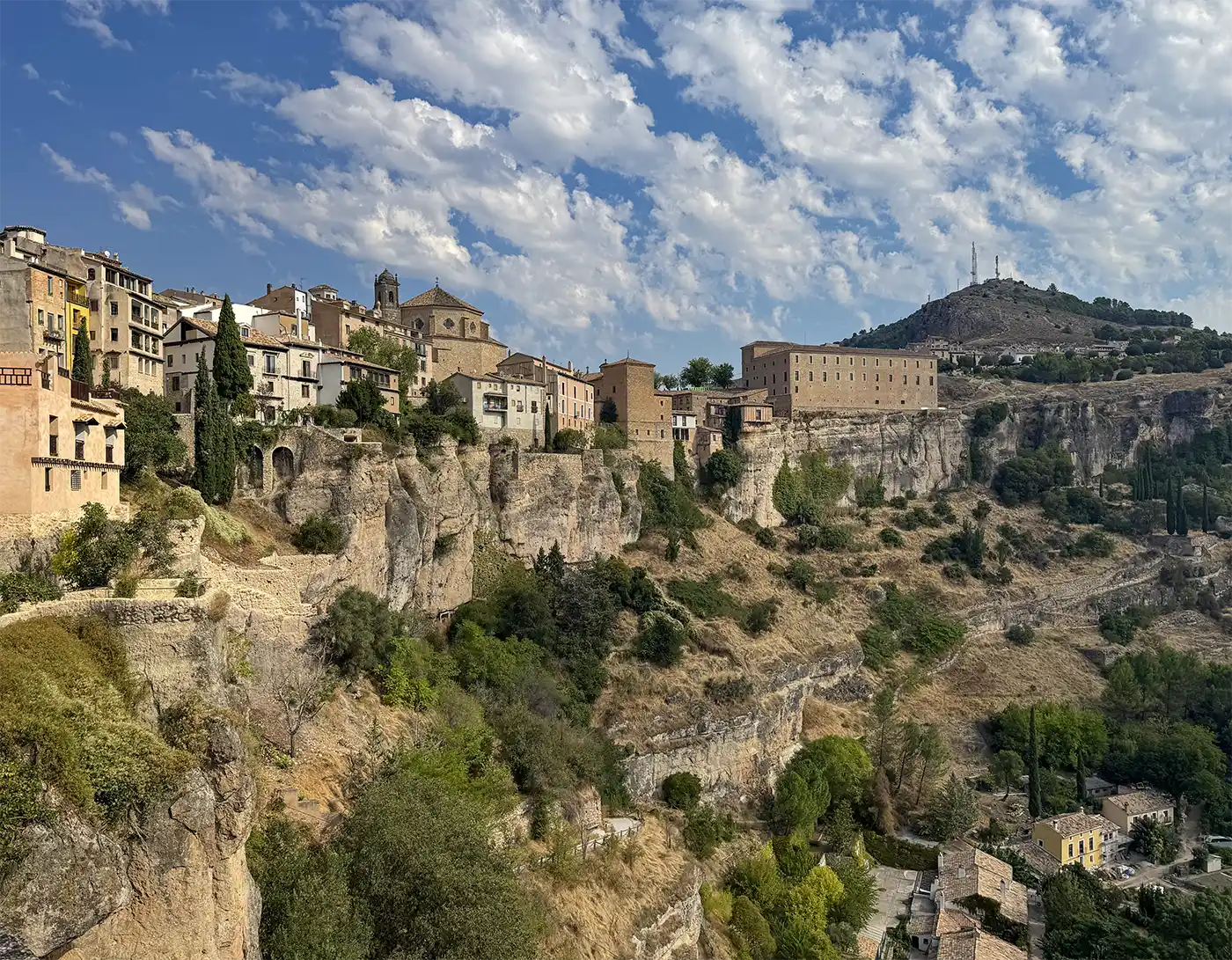 Cuenca-Schlucht-Skyline Historische Gebäude auf einer felsigen Klippe mit einem Hügel und vereinzelten Wolken im Hintergrund.