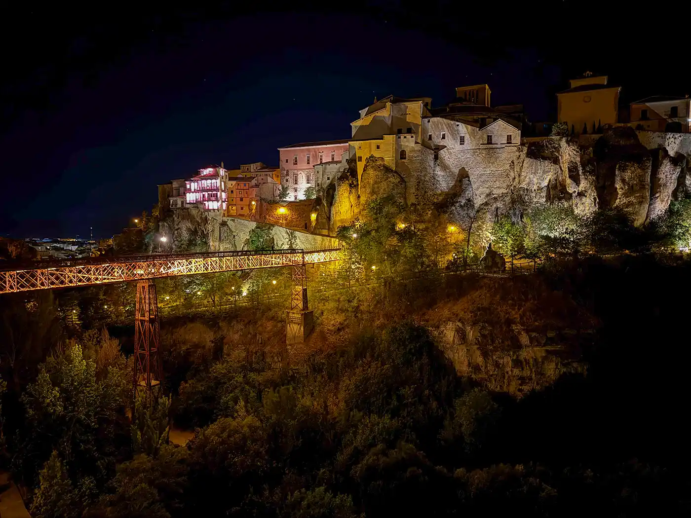 Cuenca-Schlucht-abends Nachtansicht von beleuchteten Gebäuden an einer Klippe und einer Brücke in einer historischen Stadt, umgeben von Bäumen.