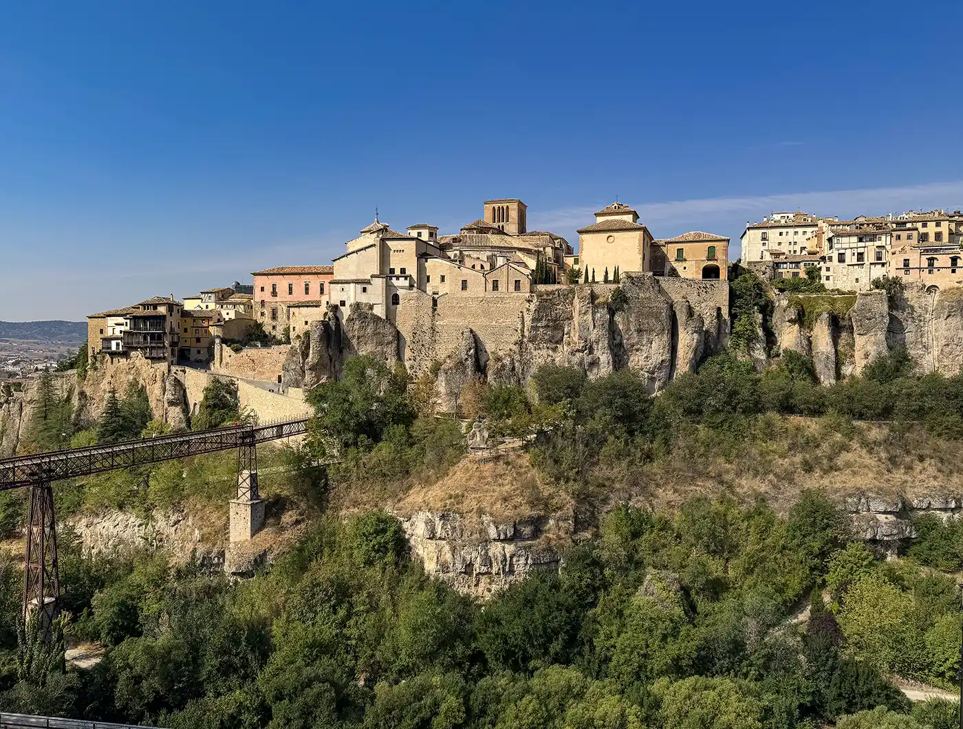 Cuenca-Spanien Ein Dorf auf einem Hügel mit Steinhäusern und einer Kirche, das hoch oben auf den Klippen über grünen Bäumen unter einem strahlend blauen Himmel thront.