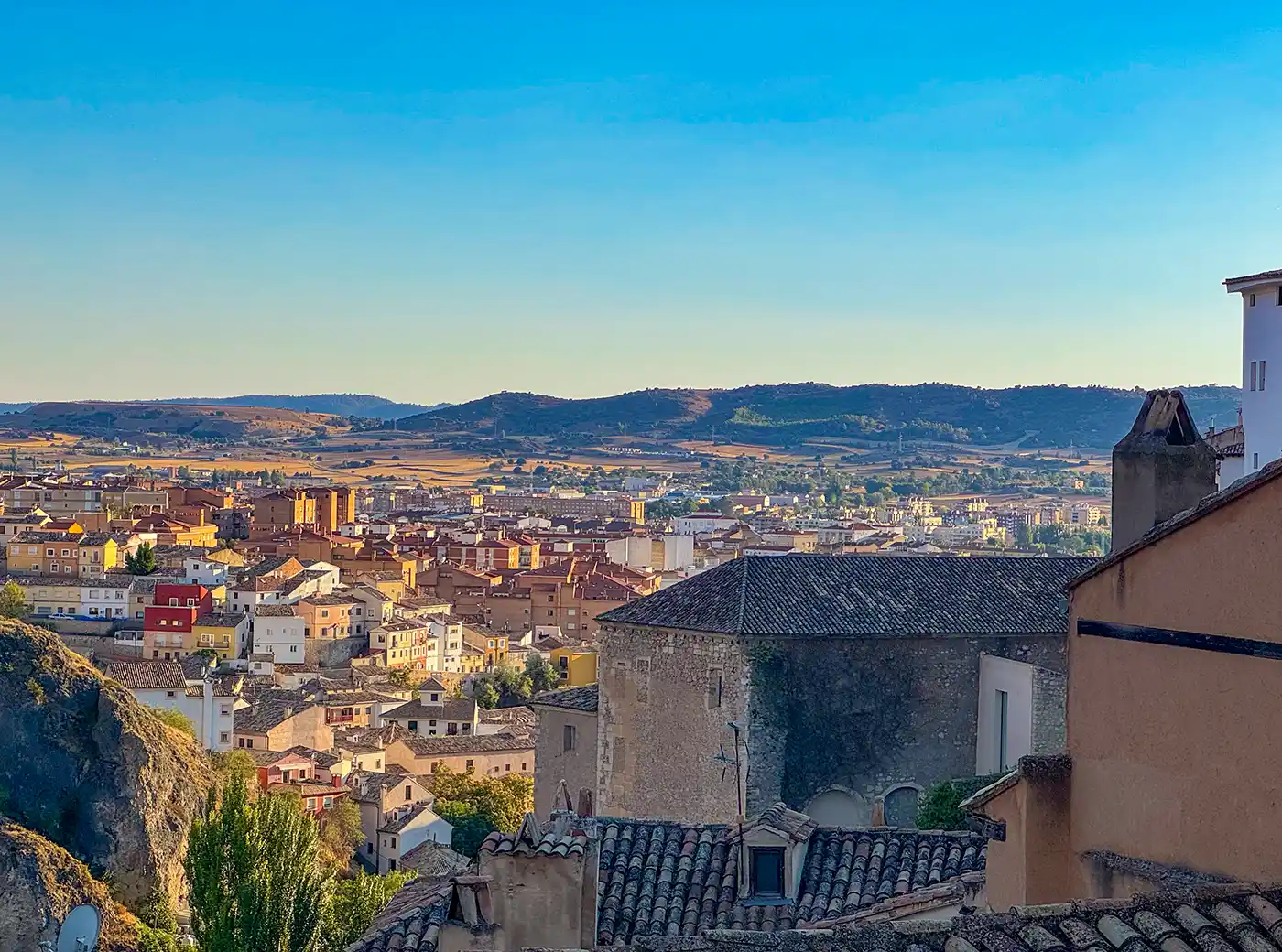 Cuenca-Unterstadt Blick vom Dach auf eine Stadt mit bunten Gebäuden und Hügeln unter einem strahlend blauen Himmel.