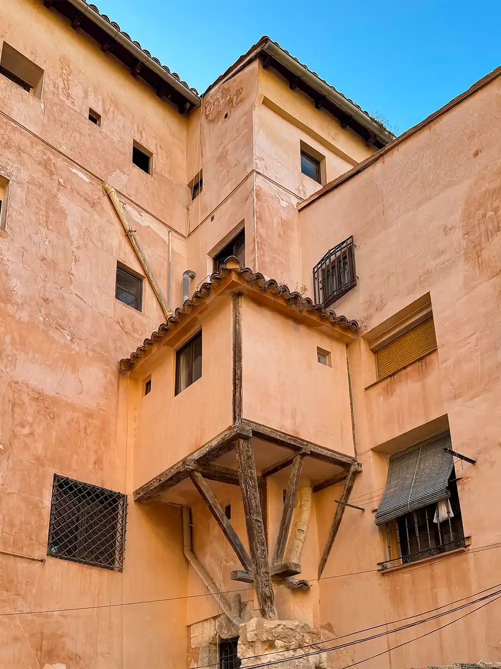 Cuenca-haengendes-Zimmer Aus einem pfirsichfarbenen Gebäude, unter dem sich Stützbalken befinden, ragt ein kleiner Holzraum hervor.