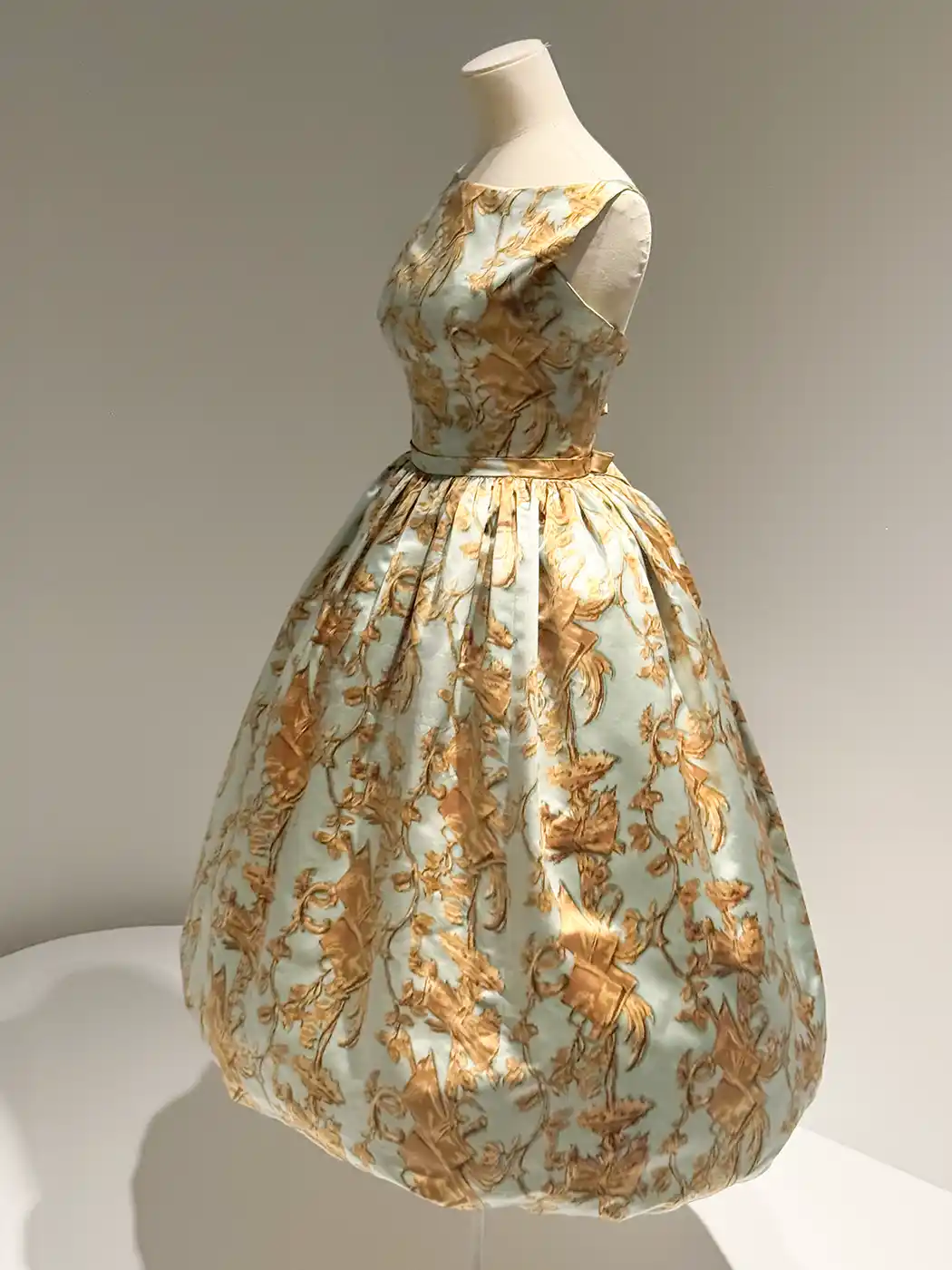 Getaria-Balenciaga-Museum-Cocktail-Kleid-1957 Schaufensterpuppe in einem ärmellosen Vintage-Kleid mit Blumenmuster und weitem Rock in Gold- und Hellblautönen.