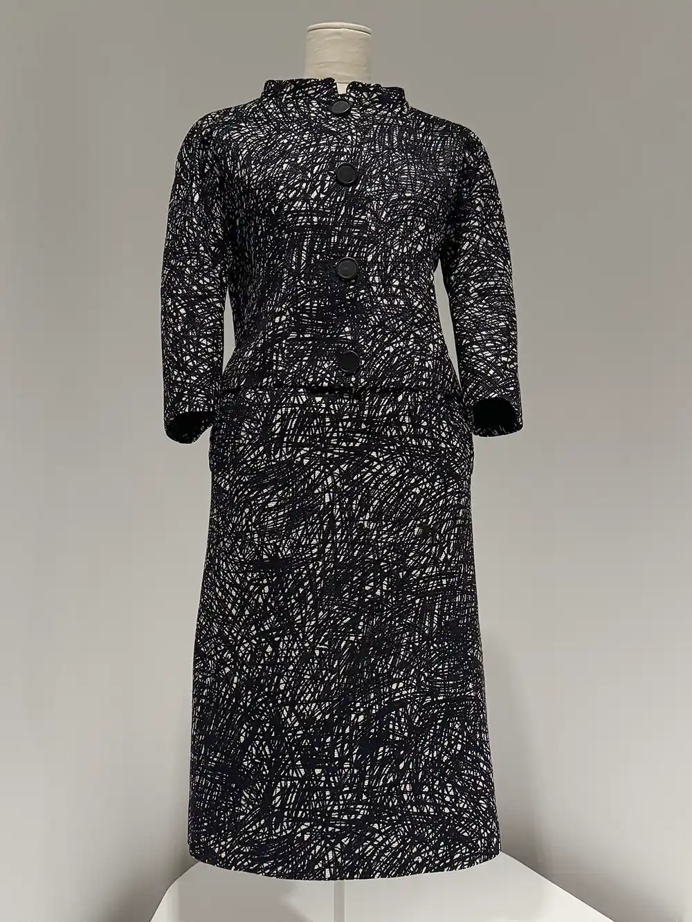 Getaria-Balenciaga-Museum-Kleid Eine Schaufensterpuppe präsentiert einen langärmeligen, schwarz-weißen Rockanzug mit Struktur und großen Knöpfen.