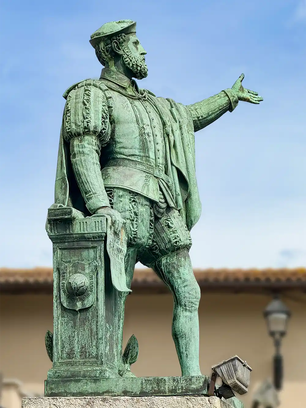 Getaria-Elkano-Denkmal-Bronze Bronzestatue eines bärtigen Mannes in historischer Kleidung, der einen Arm ausstreckt, vor blauem Himmel.