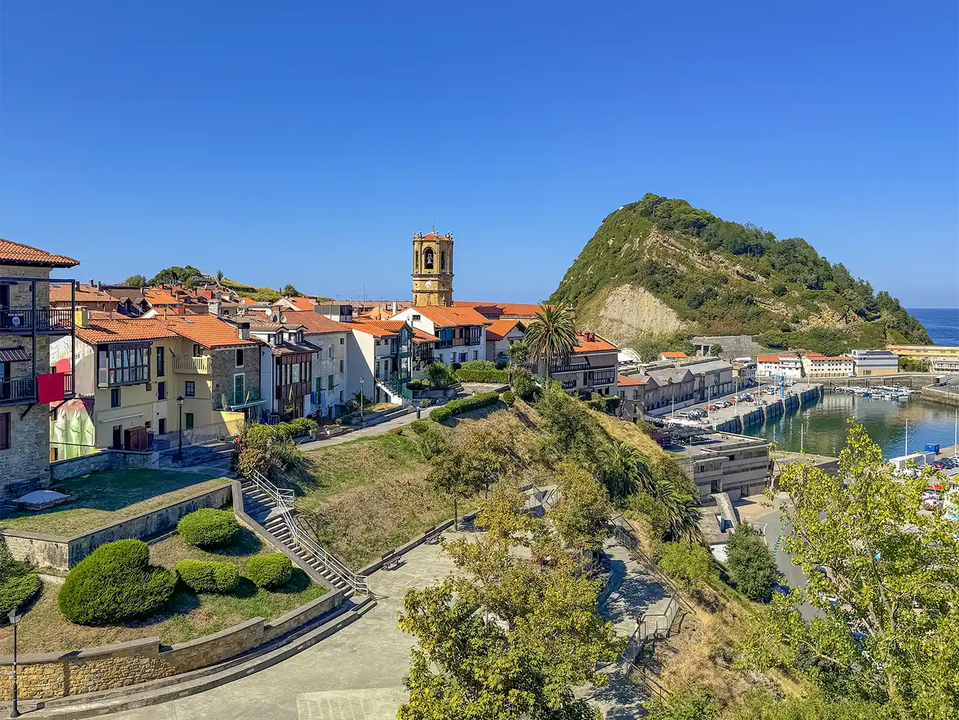 Getaria-Geheimtipp-Baskenland-Fischerdorf Blick auf ein Dorf am Meer mit Kirchturm und kleinem Berg dahinter