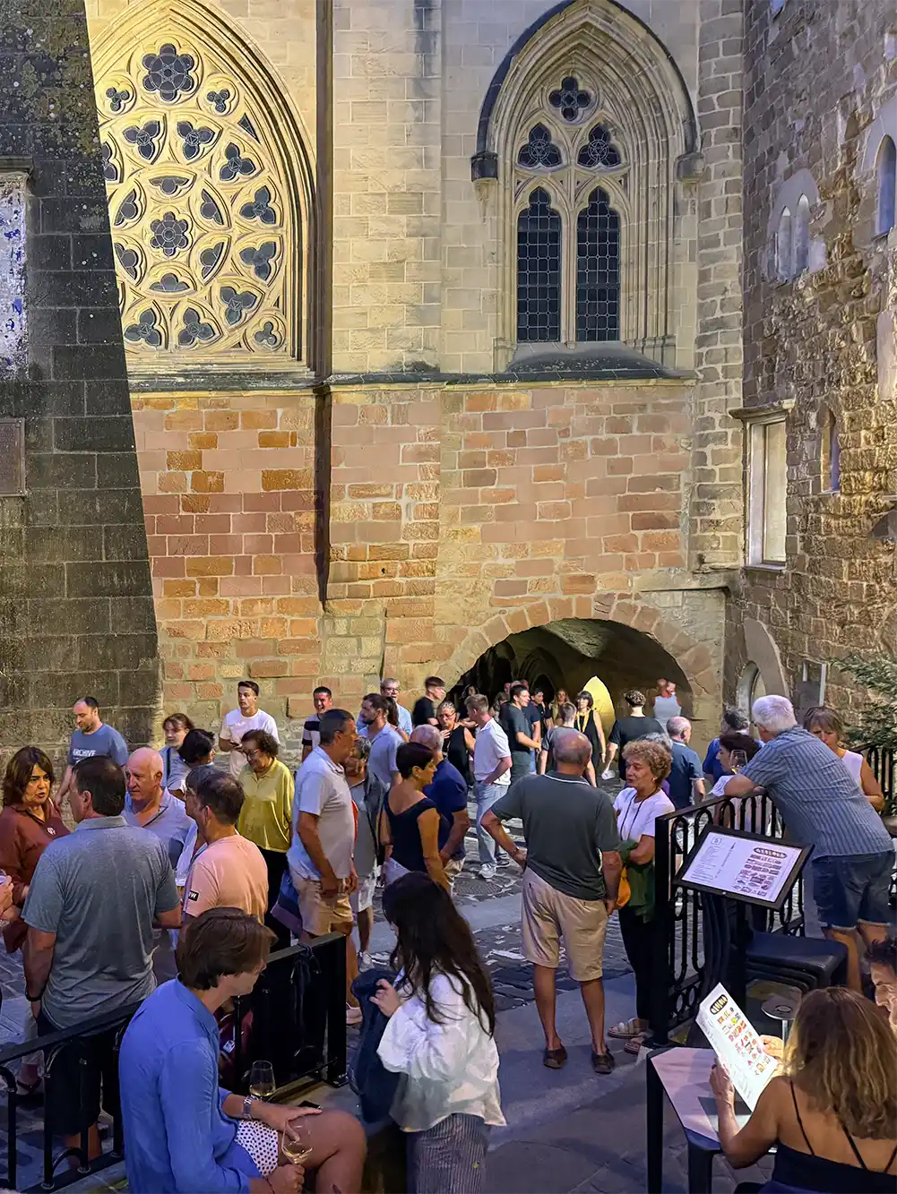 Getaria-Kirche-San-Salvador-Katrapona In der Abenddämmerung versammelt sich eine Menschenmenge in einem Innenhof in der Nähe einer großen, reich verzierten Steinkirche.