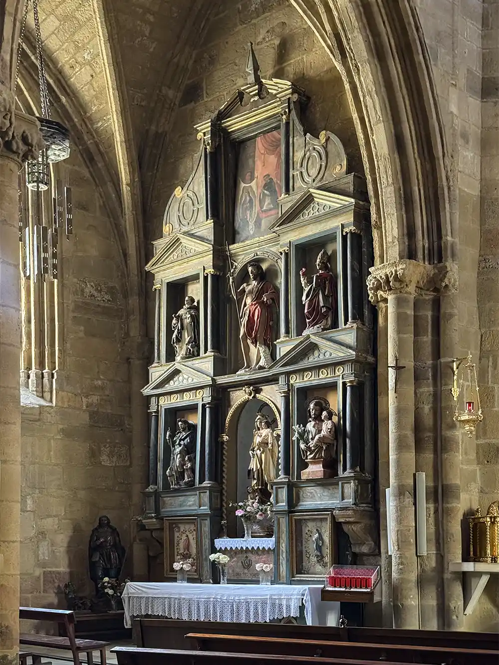 Getaria-Kirche-San-Salvador-Seitenkapelle Steinaltar in einer Kirche mit Statuen, religiösen Figuren, einer Gewölbedecke und einer Bank davor.