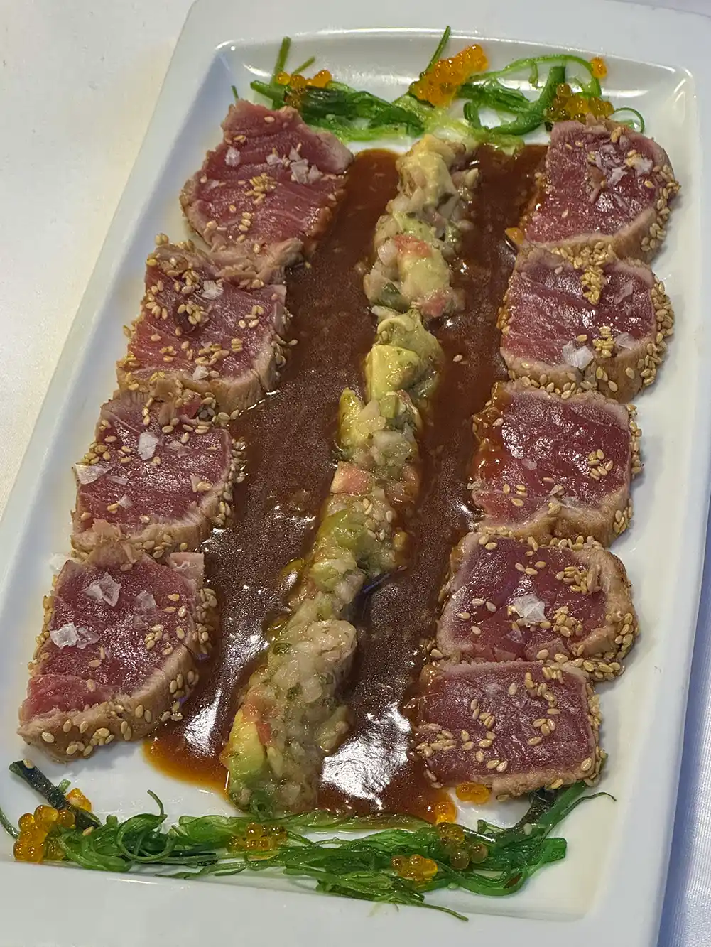 Getaria-Retsaurant-Iribar-Tunfisch Auf einem weißen Teller liegen Reihen aus angebratenen Thunfischscheiben mit Sesam, Soße, Seetang, Fischrogen und einer Avocadomischung in der Mitte.