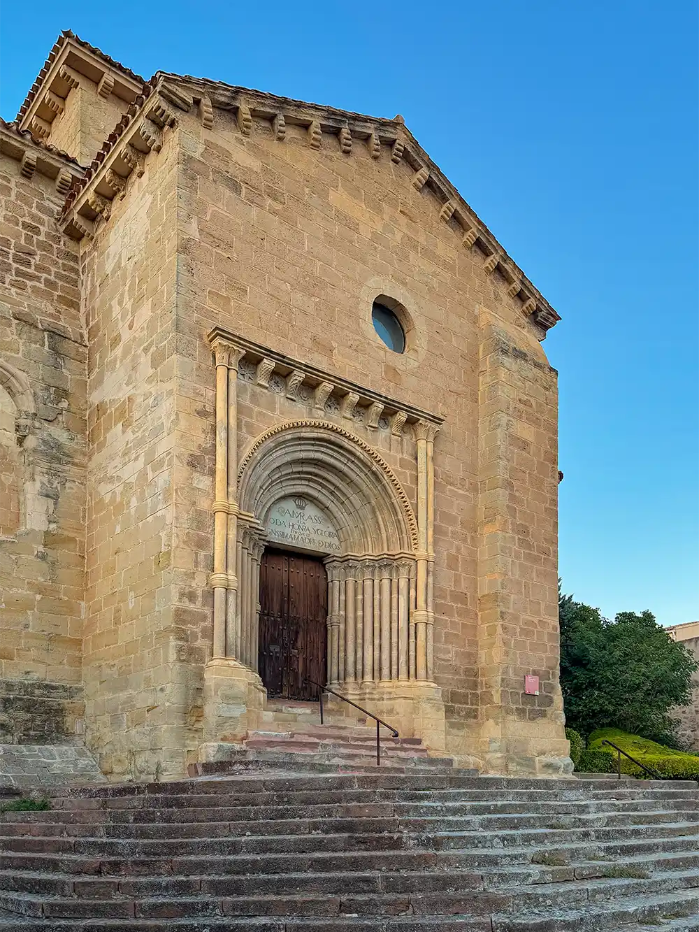 Fassade einer romanischen Steinkirche mit einem gewölbten Eingangsportal und Säulen, von einer Steintreppe aus bei Sonnenuntergang betrachtet.