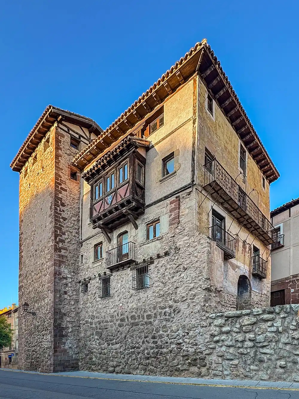 Ein Steinhaus mit einem Turm, einem Holzbalkon und kleinen Fenstern vor dem Hintergrund eines strahlend blauen Himmels.