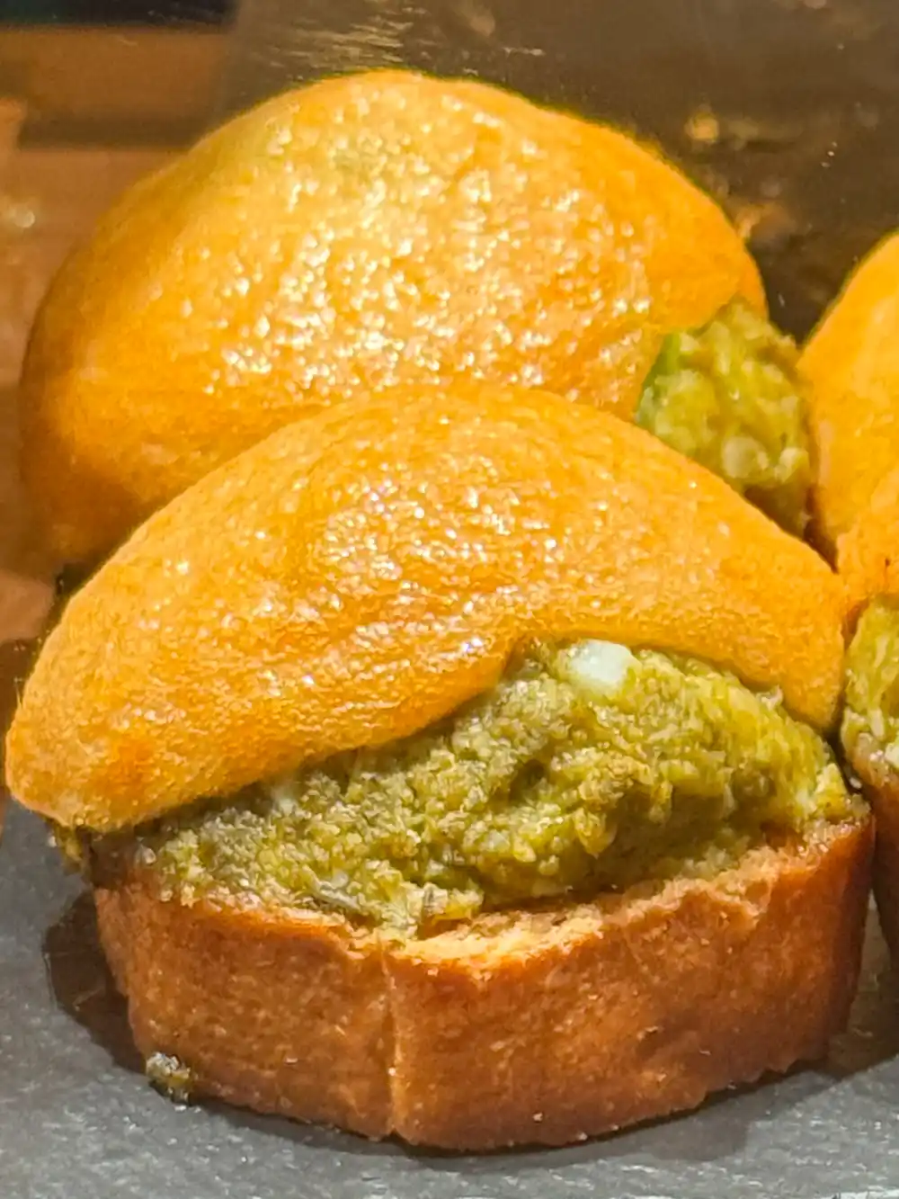Goldbraune Muffins mit grüner Füllung, präsentiert auf einem dunklen Untergrund.