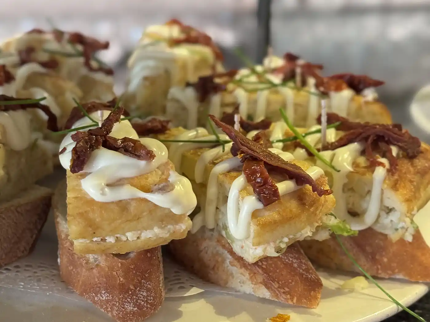 Tapas mit spanischem Omelett auf Baguette, garniert mit Mayonnaise und sonnengetrockneten Tomaten, serviert in den besten Pintxo-Bars.