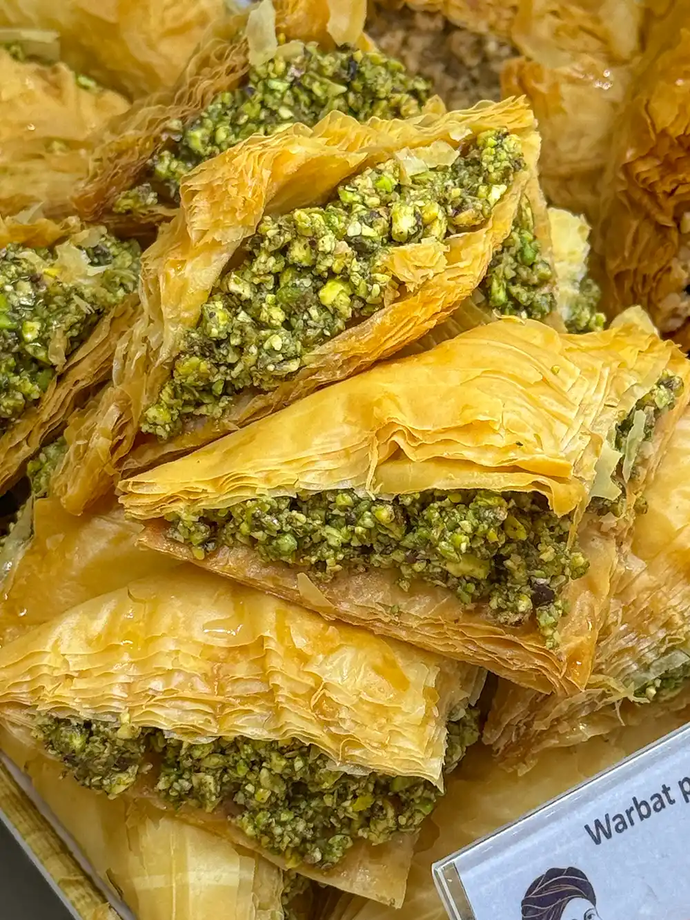 Warbat-Pistazien Dreieckige Baklava-Stücke mit blättrigen Teigschichten und einer großzügigen Pistazienfüllung, die übereinandergestapelt sind.
