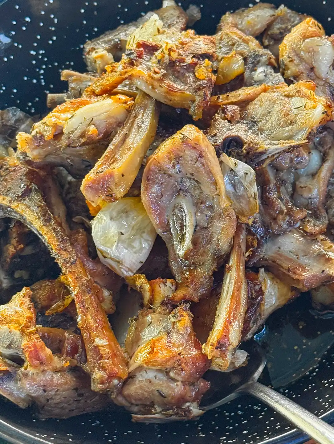 Gebratene Lammkoteletts mit Knoblauchzehen in einer dunkel gesprenkelten Pfanne.