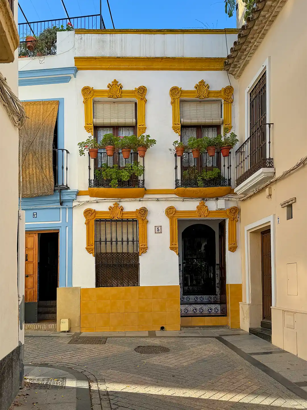 Cordoba-Altstadtgasse Weißes Gebäude mit gelben Zierfensterrahmen, Topfpflanzen auf den Balkonen und einem gefliesten Eingangsbereich.