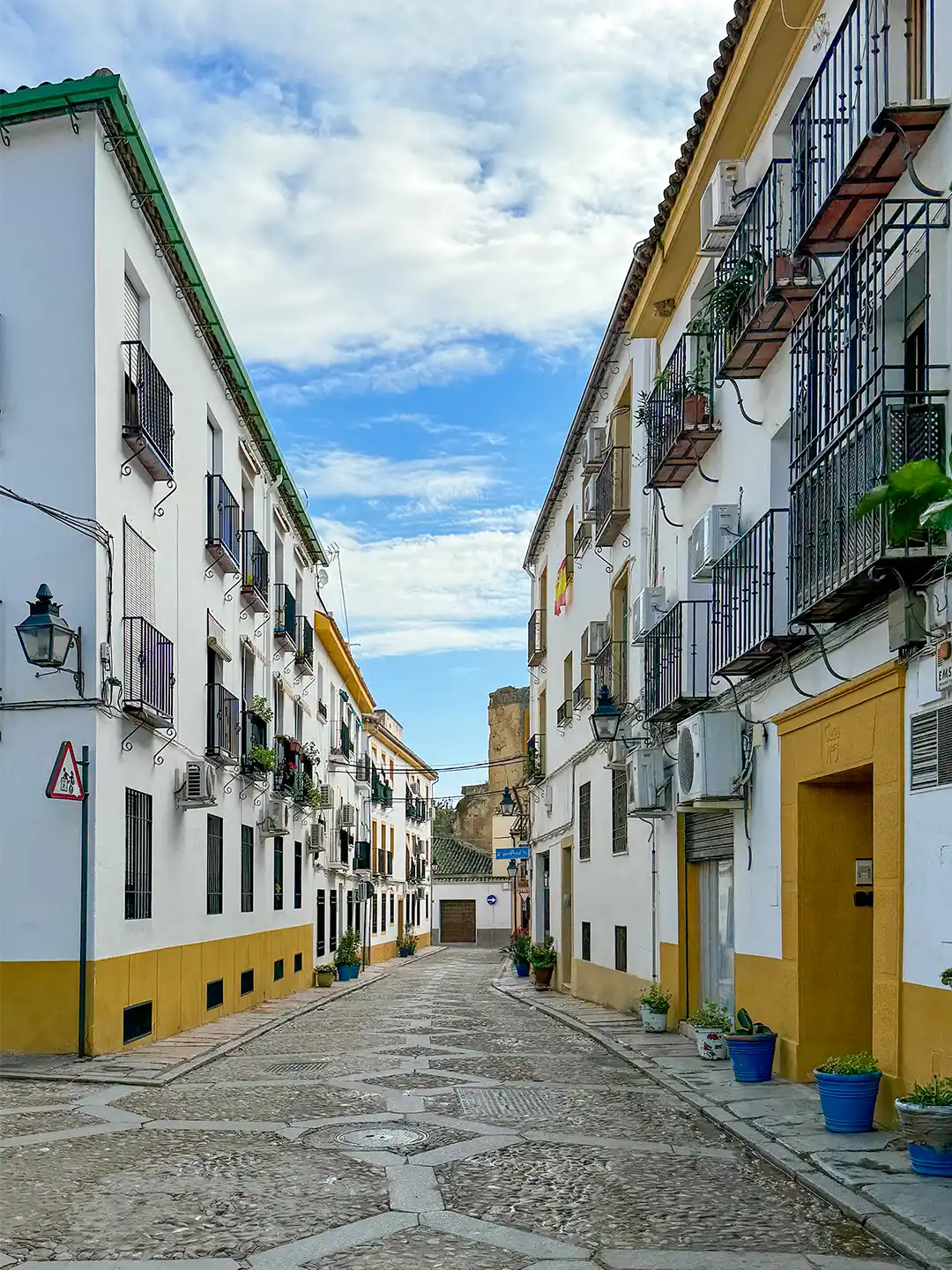 Cordoba-Juderia Eine schmale Kopfsteinpflasterstraße zwischen zwei weiß-gelben Gebäuden in einer spanischen Stadt.