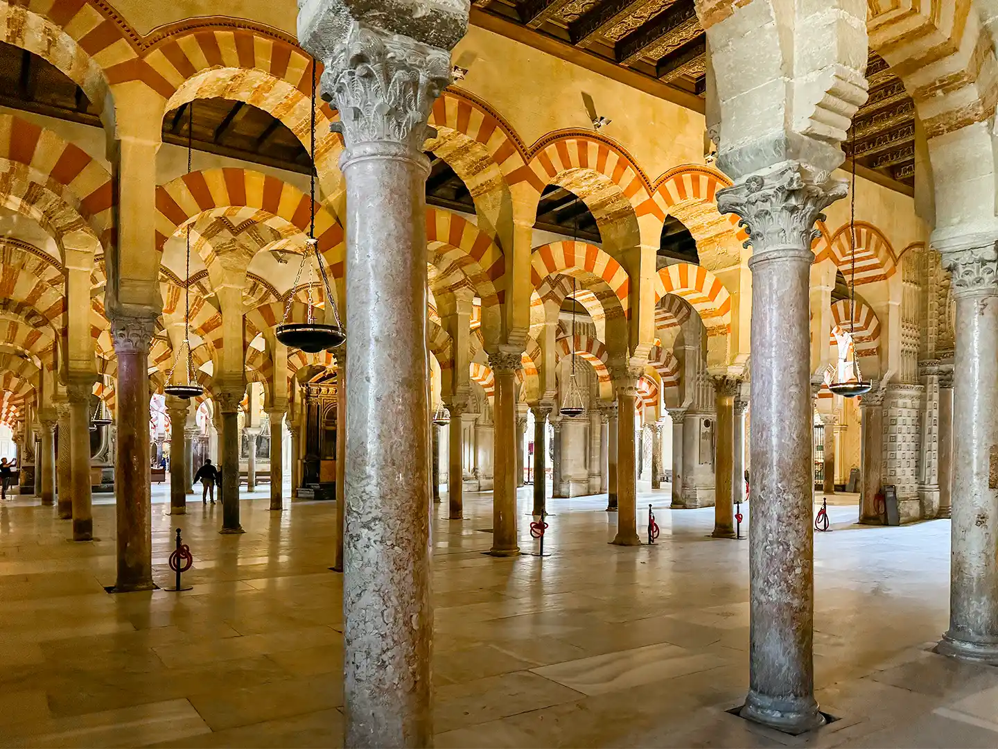 Cordoba-Mezquita-Saeulenwald Innenansicht der Moschee-Kathedrale von Córdoba mit Reihen aus Steinsäulen und rot-weiß gestreiften Bögen.