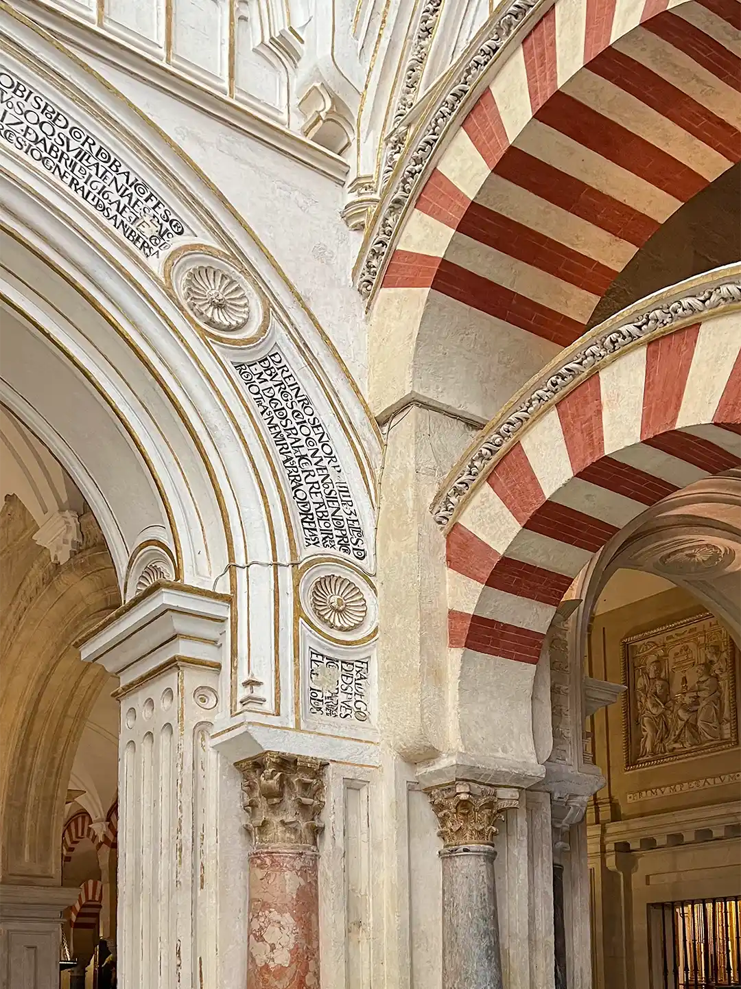 Cordoba-Mezquita-gotisch-maurische-Boegen-2 Bögen mit rot-weiß gestreiften Keilsteinen und lateinischen Inschriften, die in die Steinsäulen eingemeißelt sind.