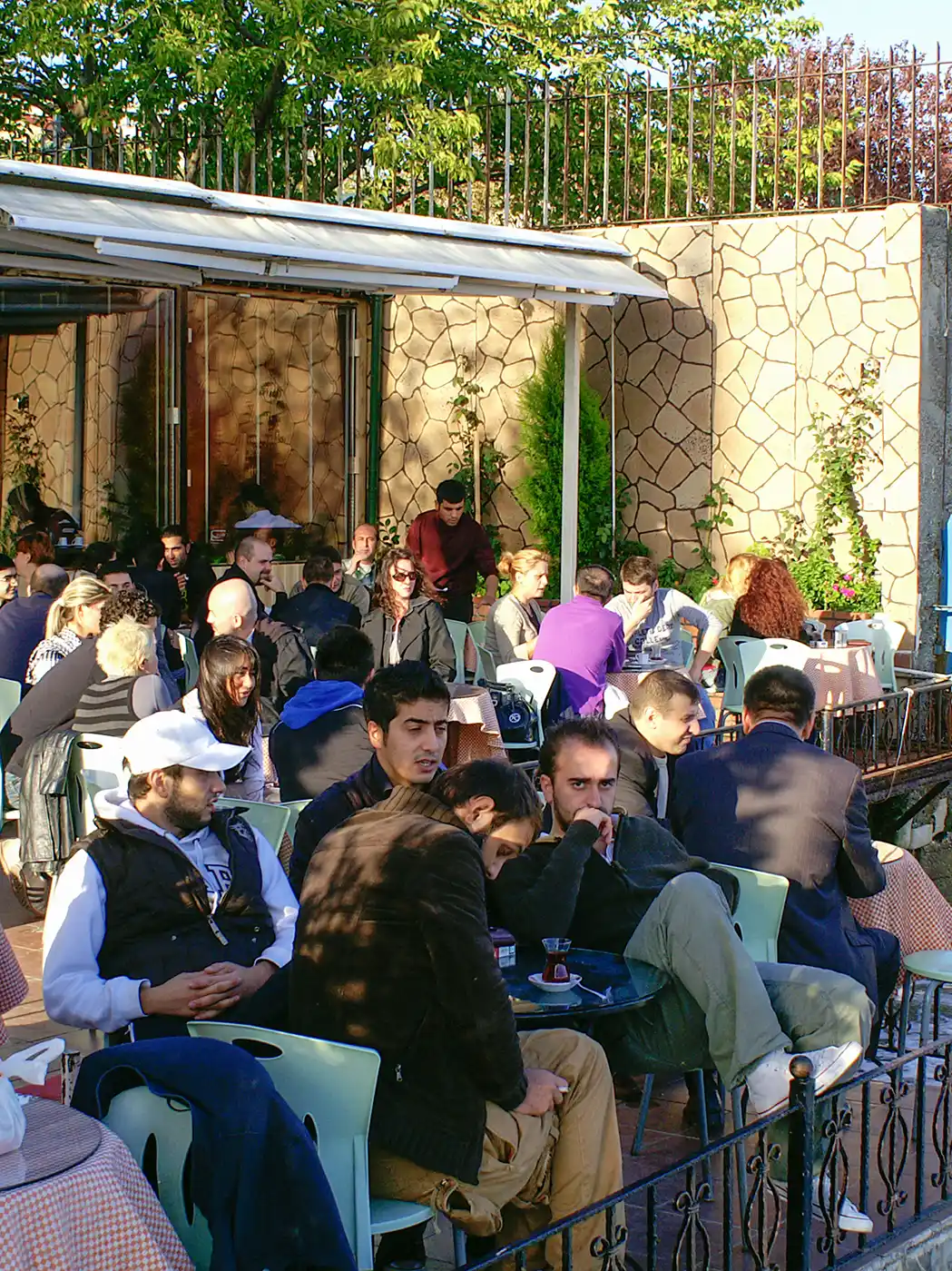 Istanbul-Cafe-Bosporus Eine gut besuchte Caféterrasse im Freien, auf der Menschen an Tischen sitzen.