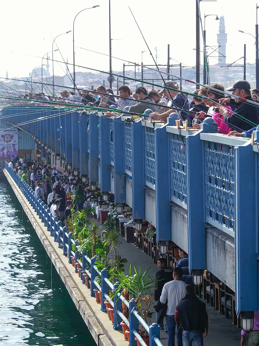 Istanbul-Galata-Bruecke-Angler Viele Menschen stehen an der Brüstung einer Brücke und angeln mit langen Ruten im Wasser darunter.
